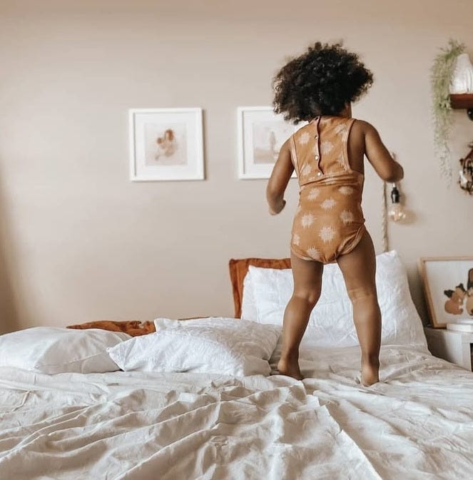 Child jumping on a bed, facing away from the camera.