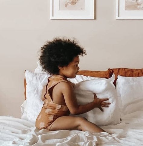 Child in swimsuit on a bed with pillows.