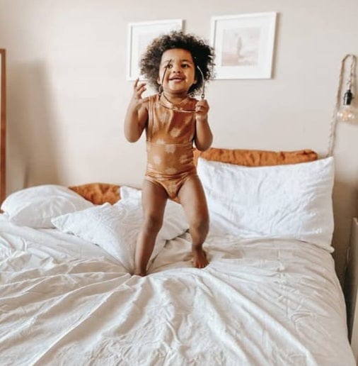 Smiling toddler jumping on a bed.