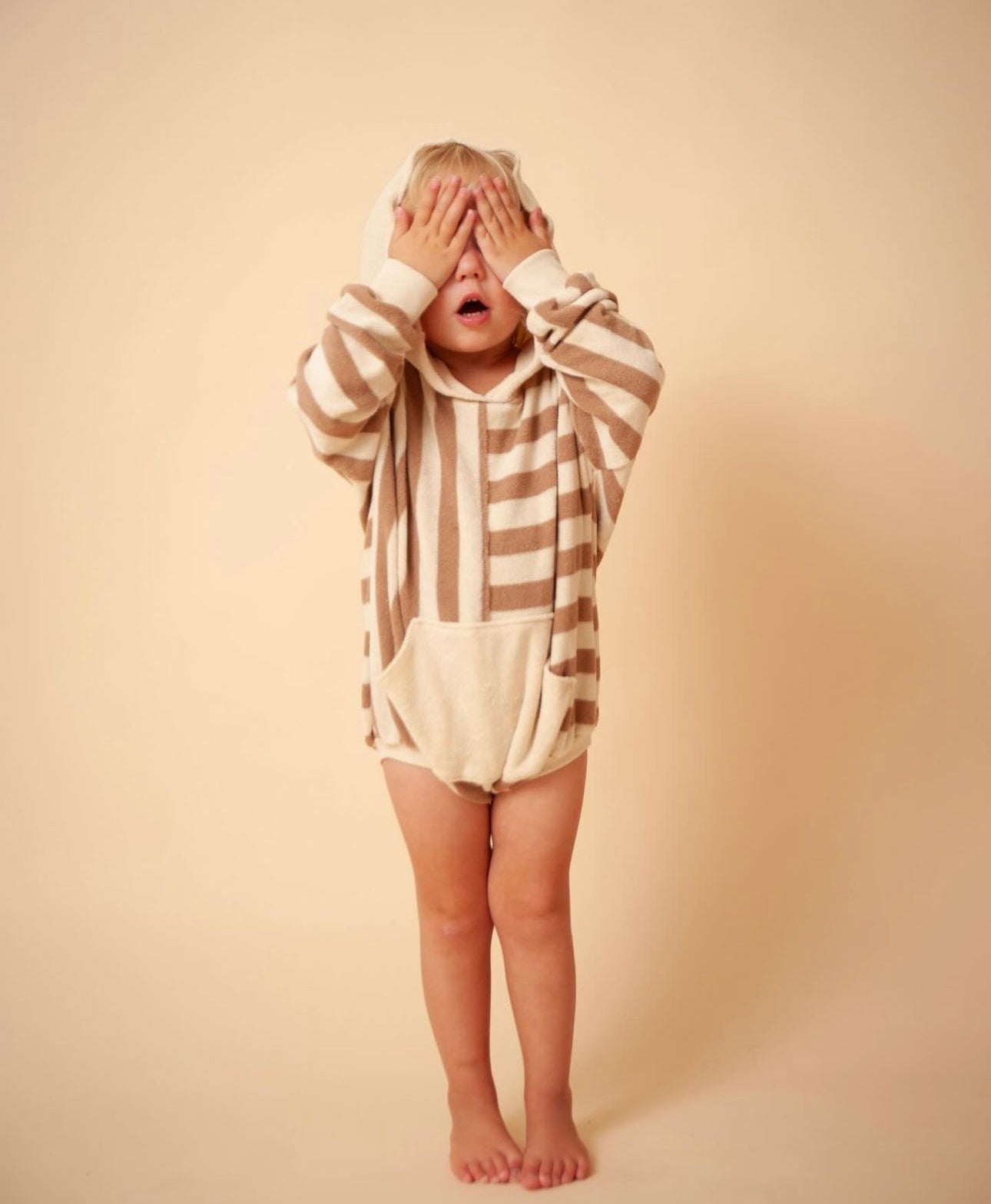 Child in striped hoodie covering eyes