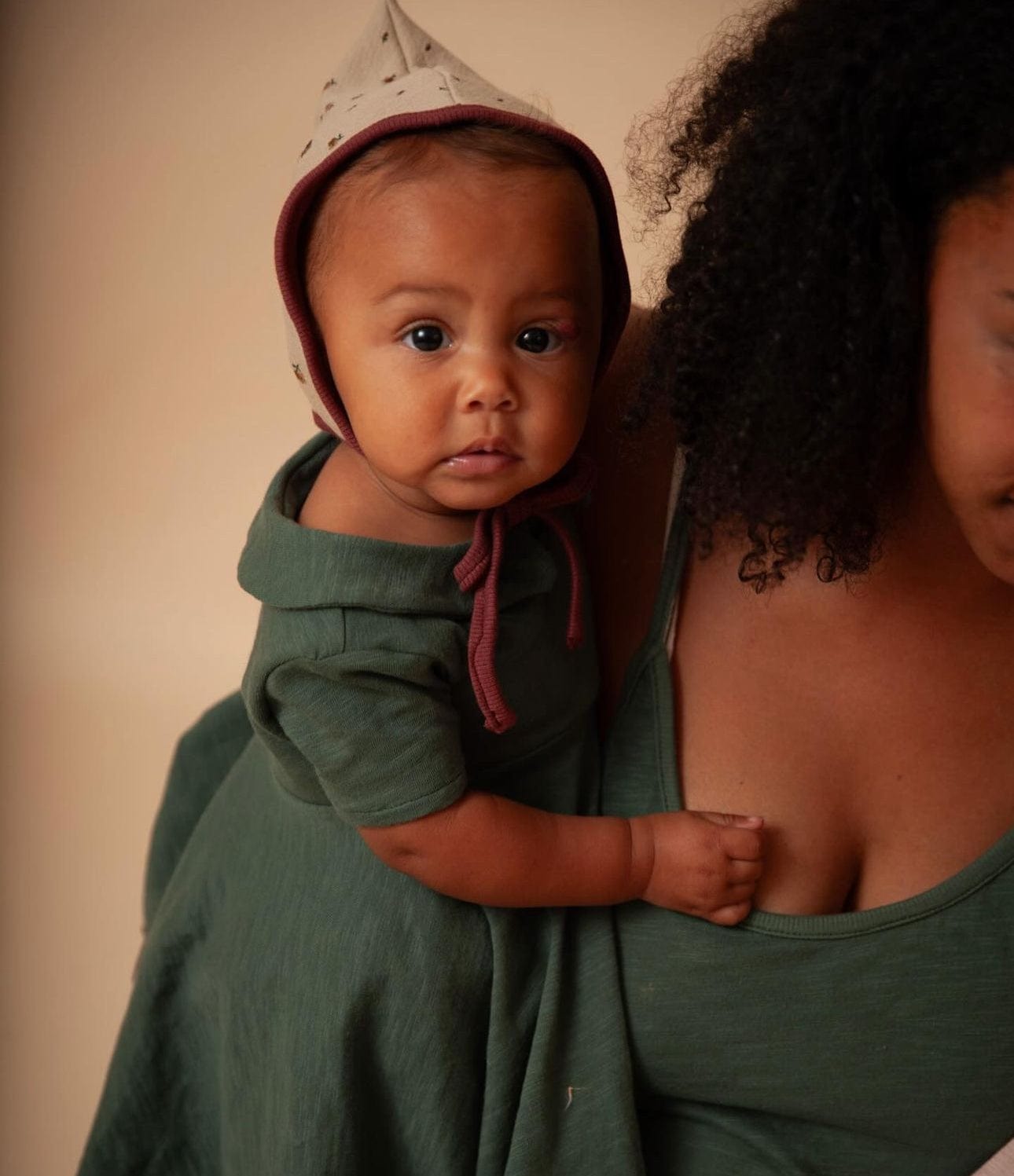Baby in green dress and hat held by mother