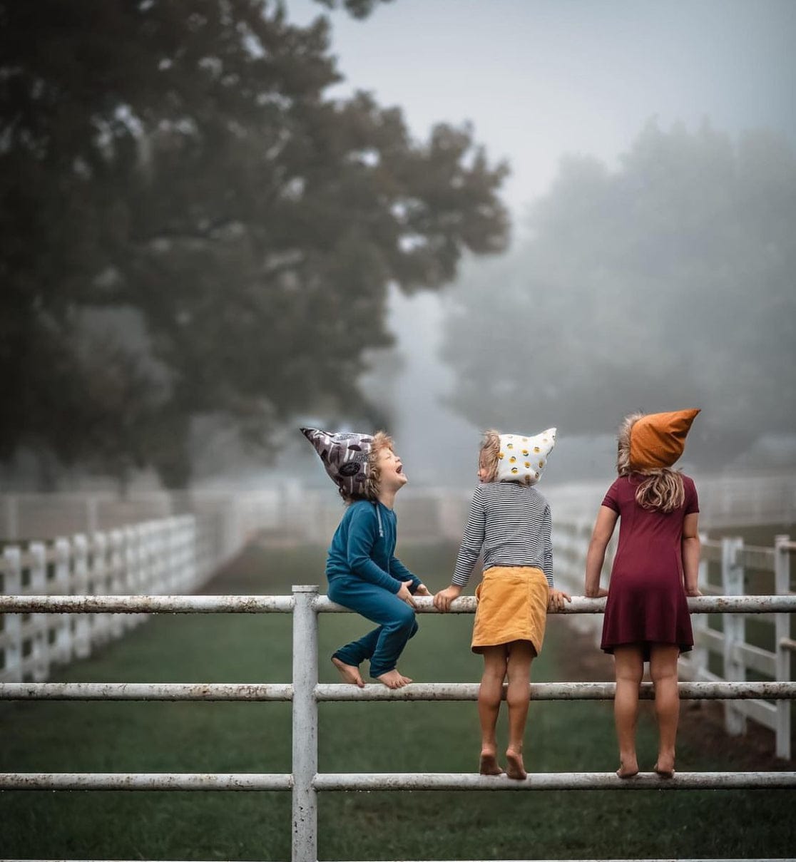 Children in whimsical hats on fence, foggy day