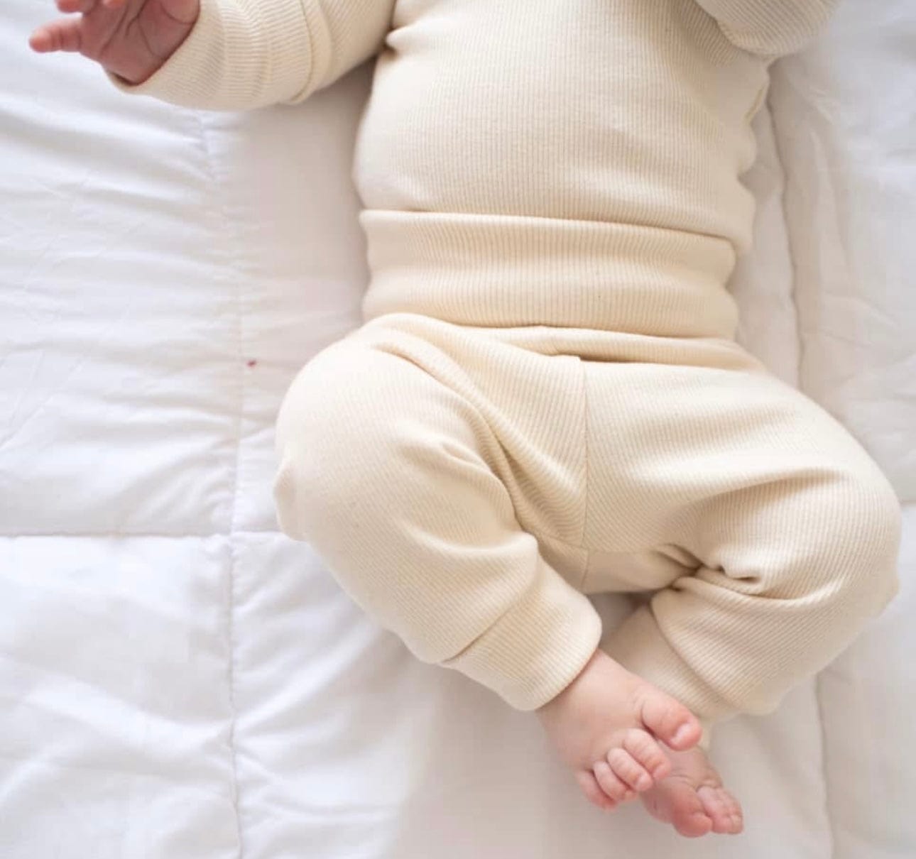 Baby in cream-colored outfit on white blanket