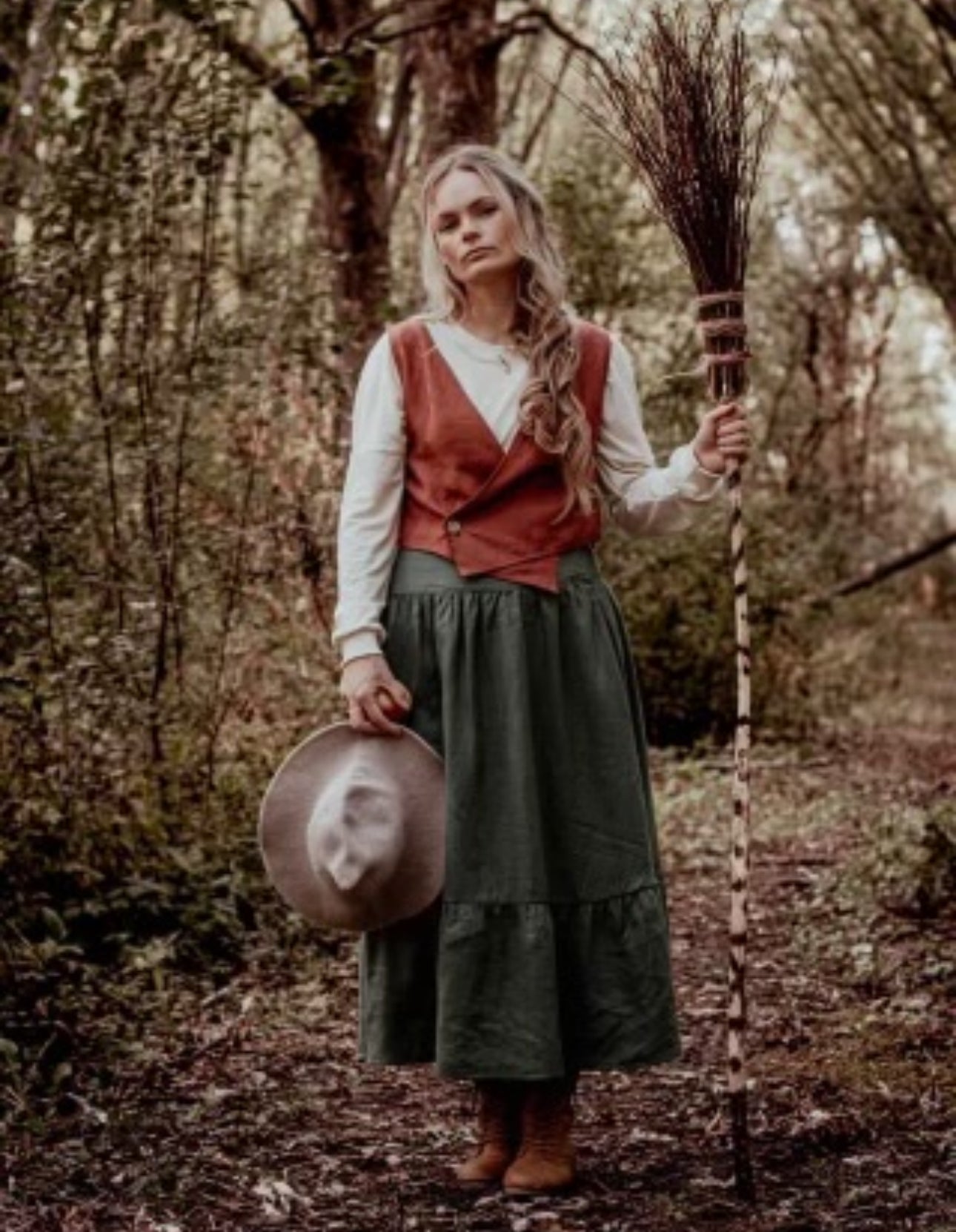 Woman in forest holding broom and hat