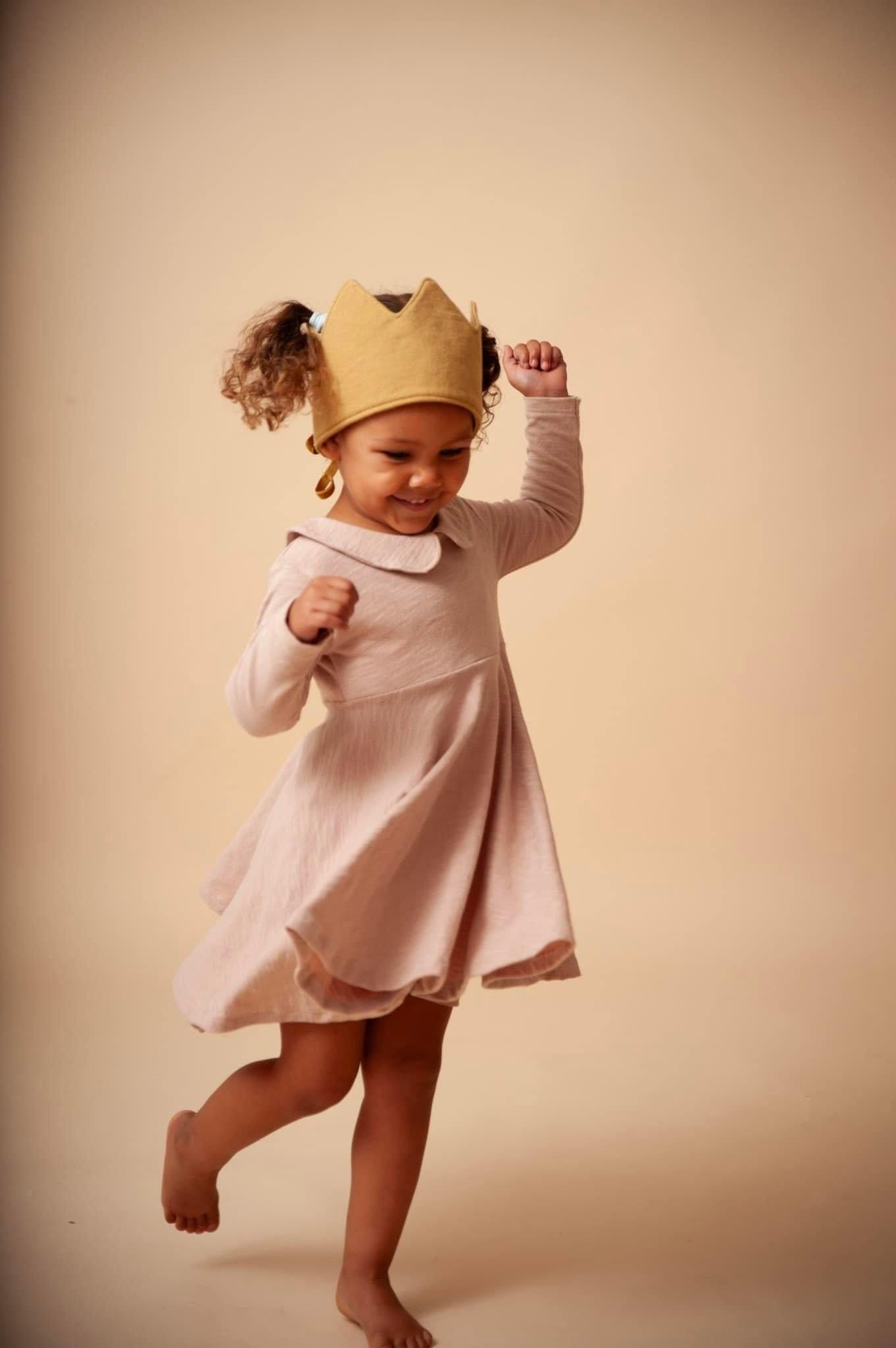 Girl wearing crown and dress, dancing.