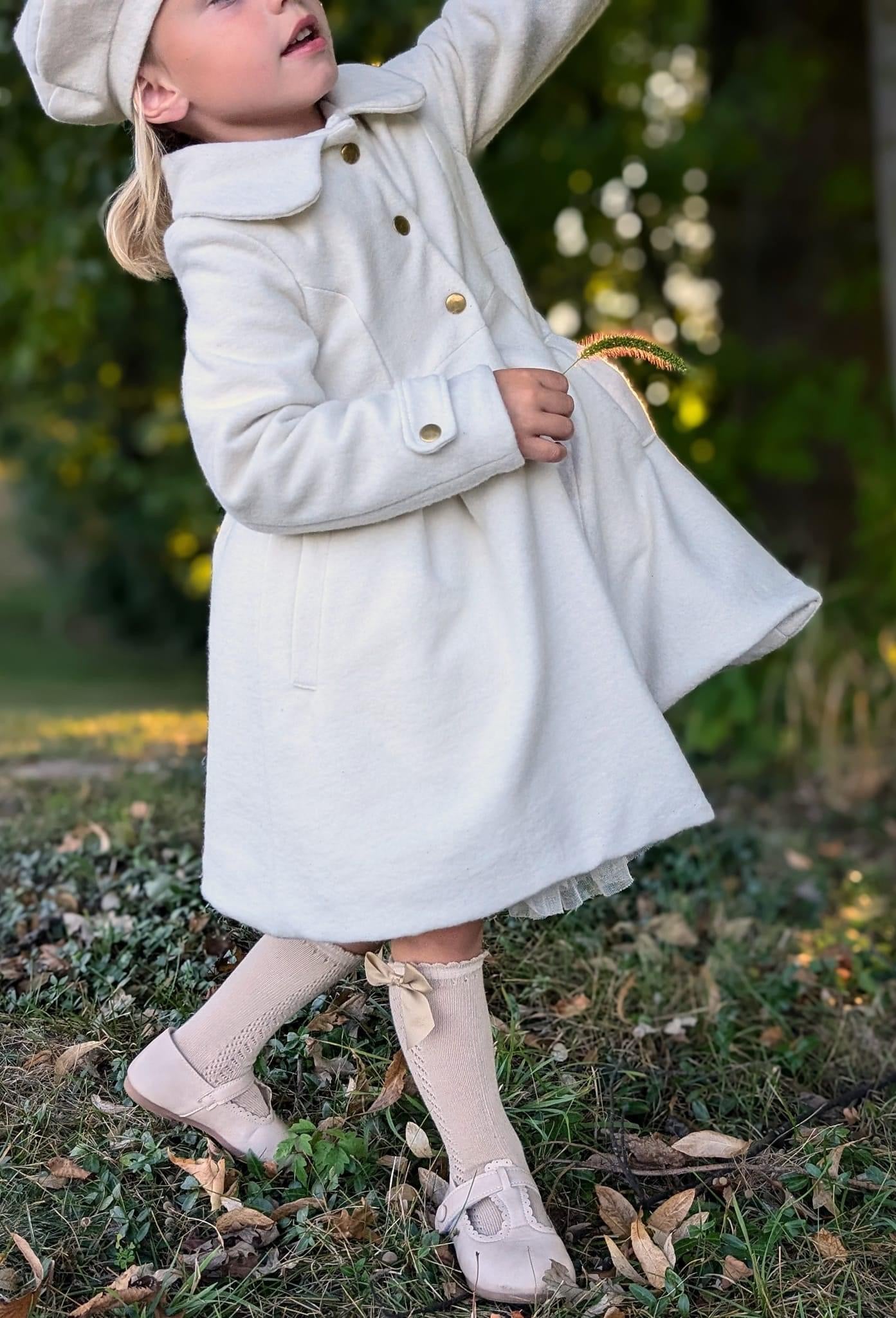 Girl in white coat and beret outdoors.