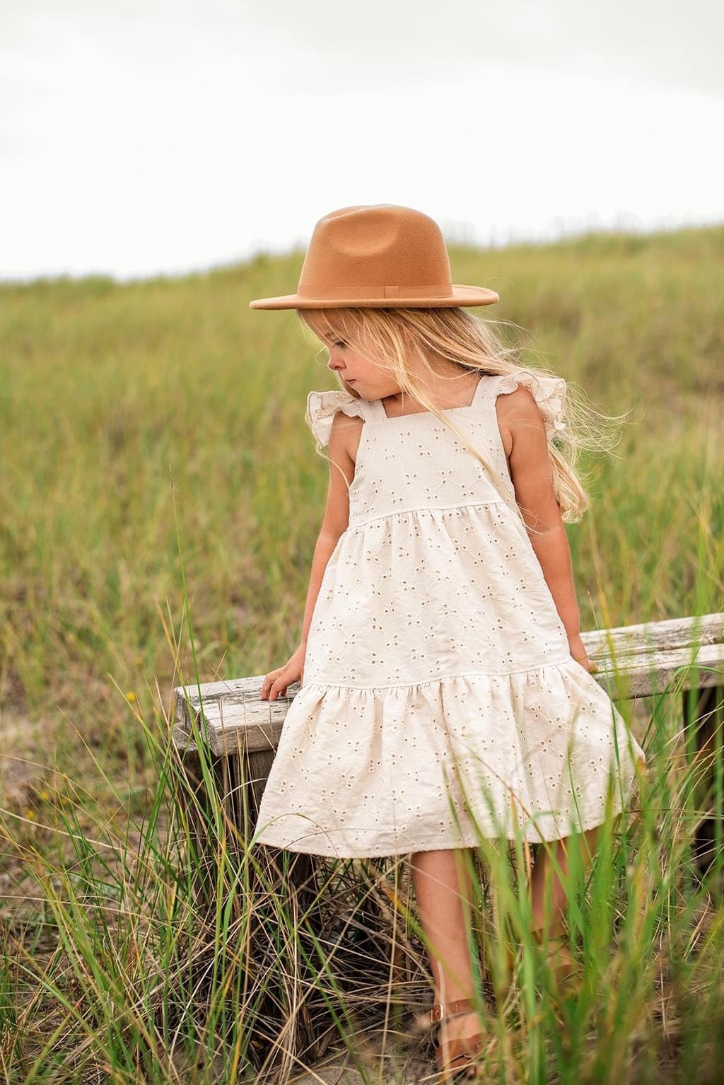 Girl in a hat and dress standing in tall grass.