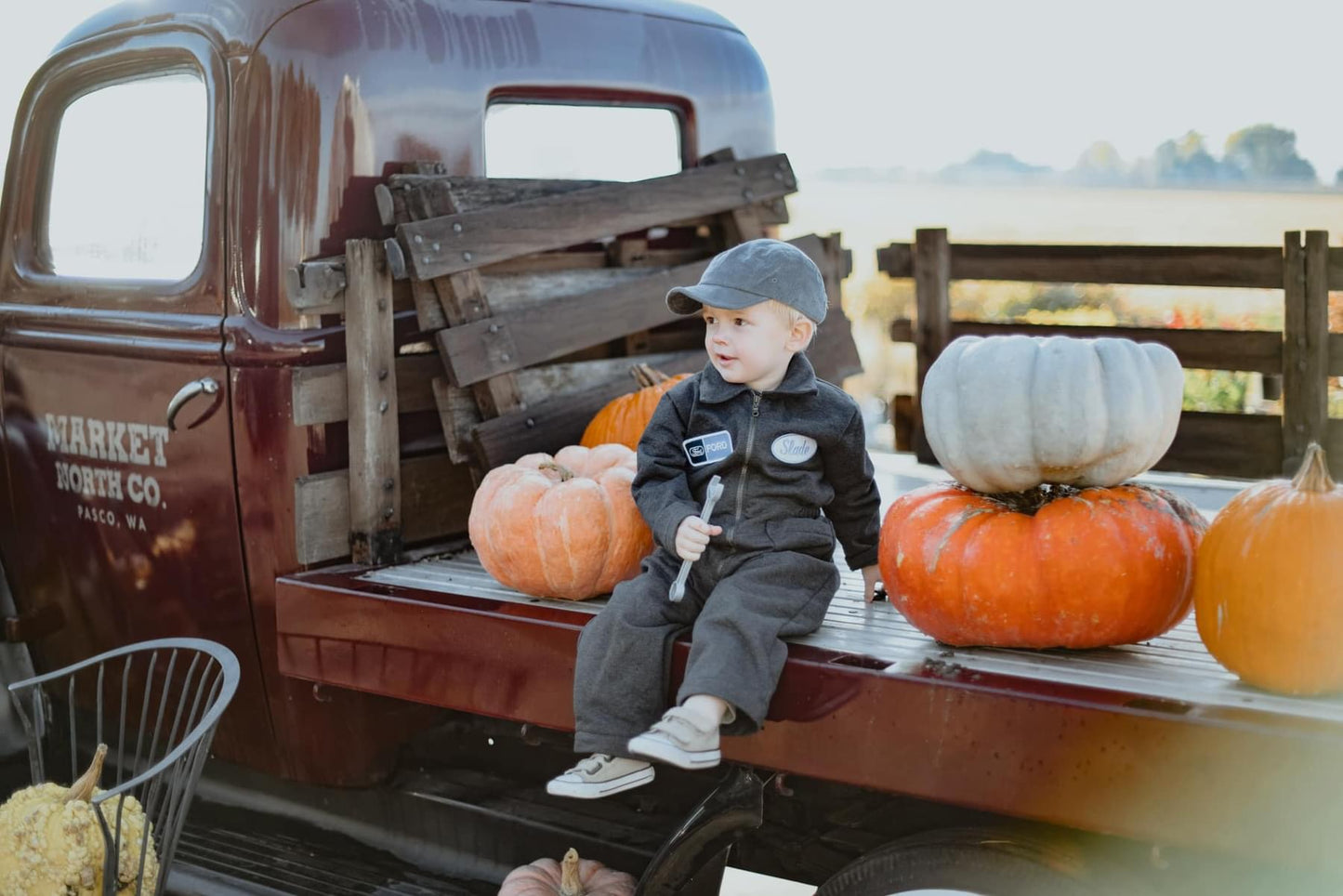 Boy sitting on truck bed with pumpkins.