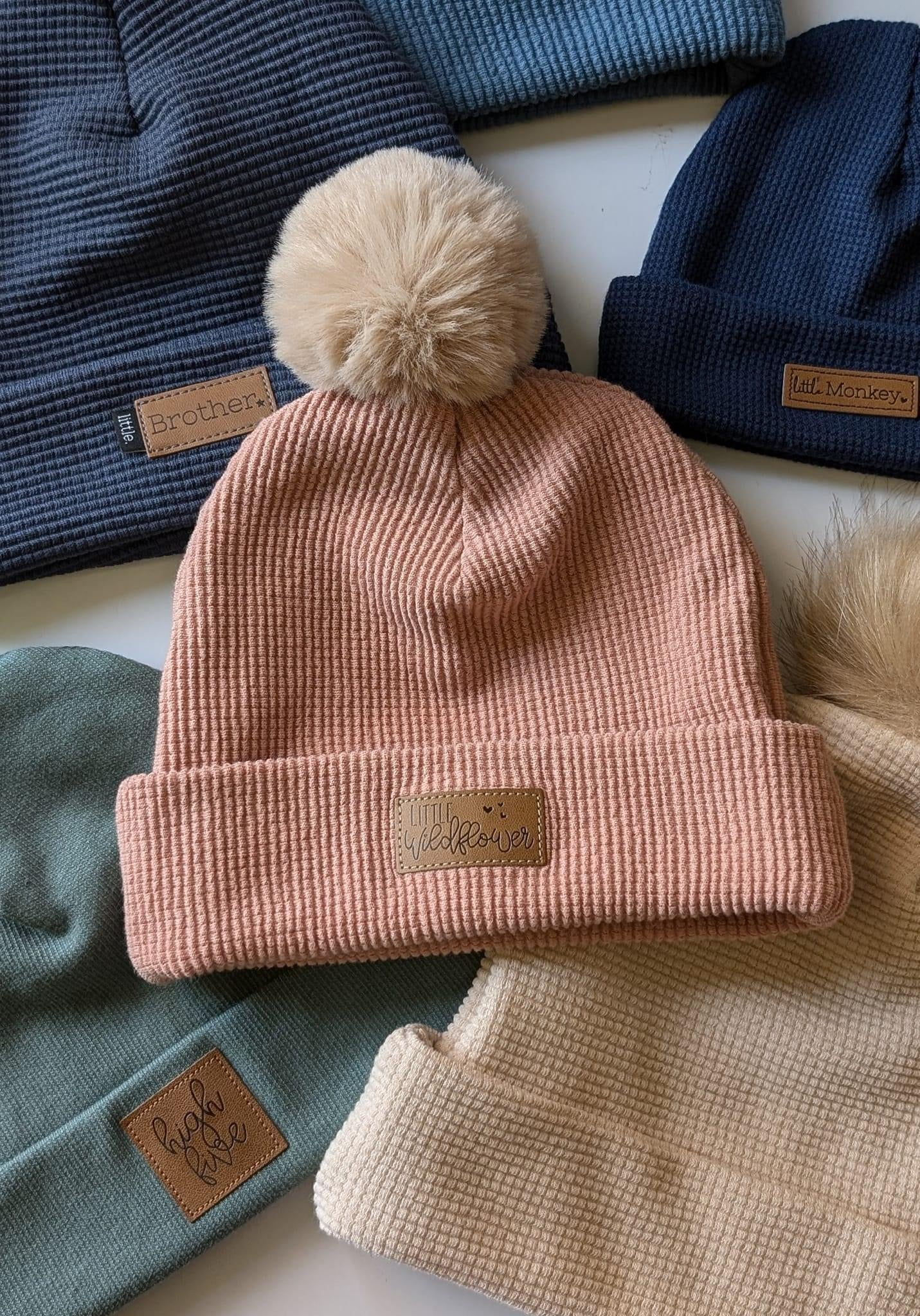 Pile of colorful knit beanies with pompom.