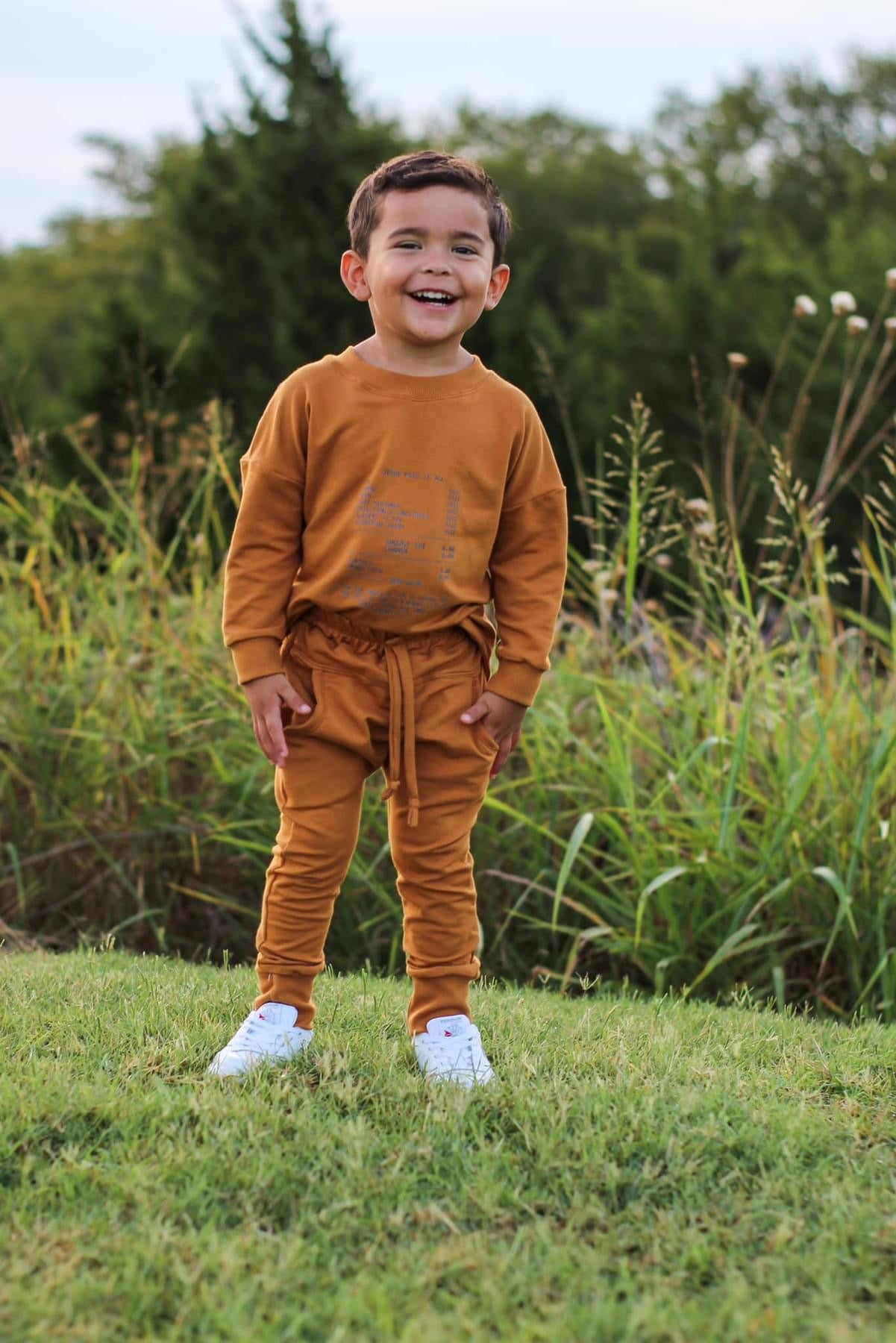 Smiling child wearing brown sweatsuit and white shoes.