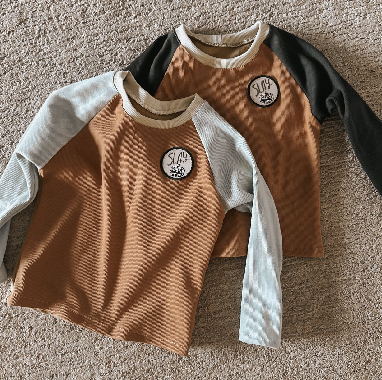 Two brown and blue raglan shirts with SLAY patches.