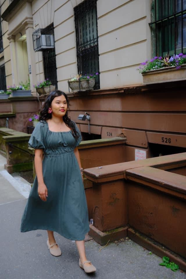 Woman in green dress walking on sidewalk.