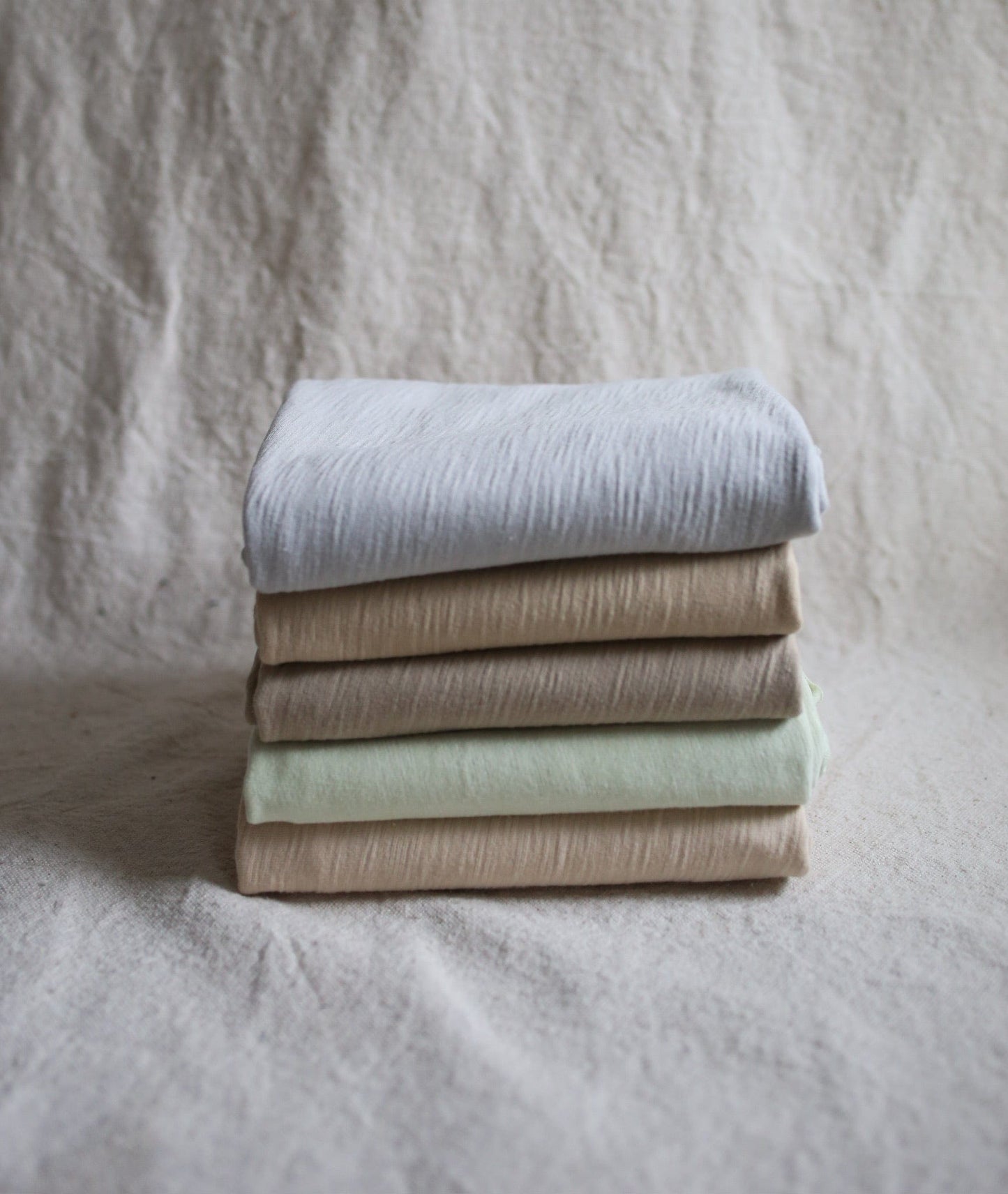 Stack of folded fabric in various neutral colors.