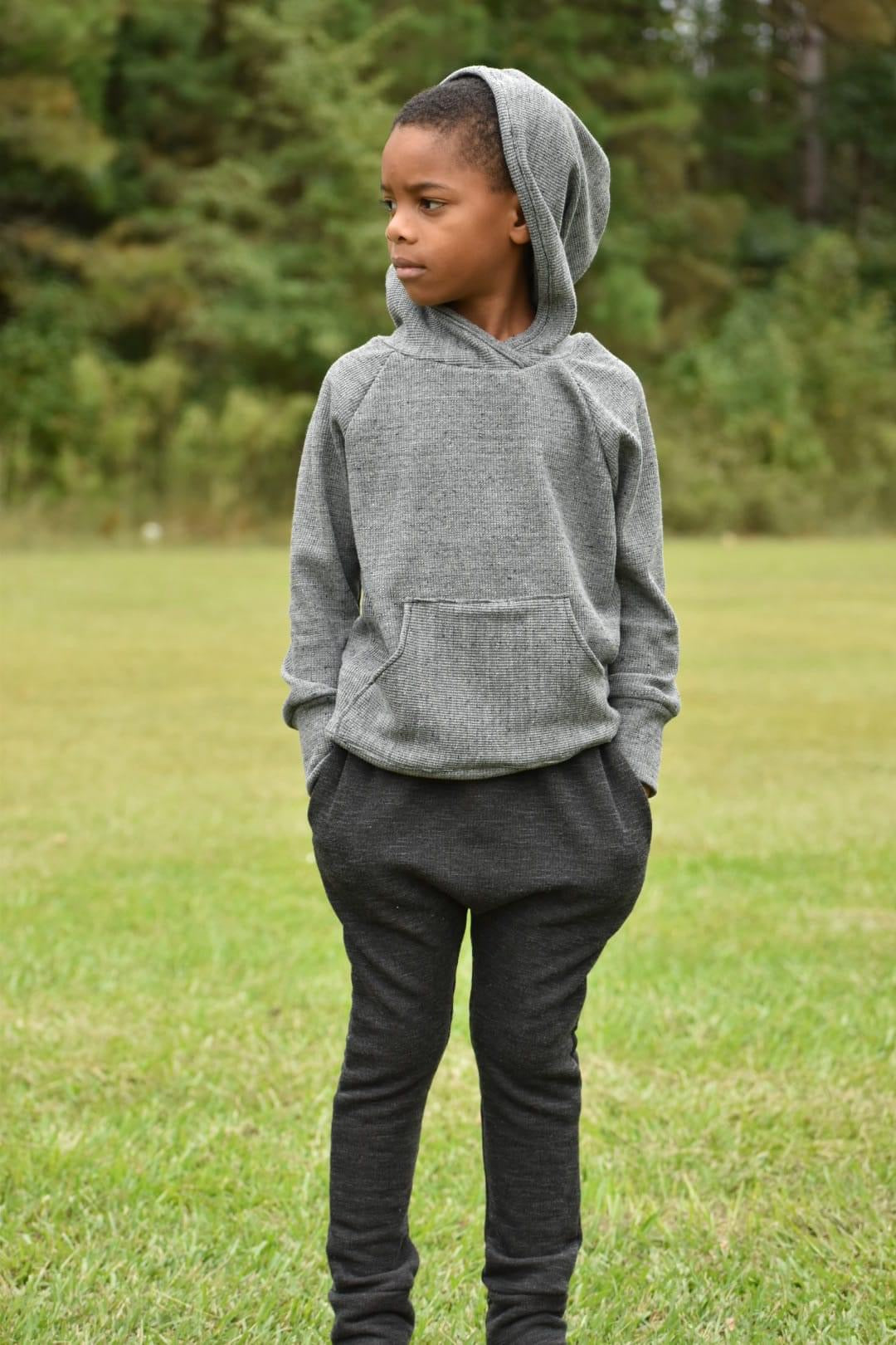 Boy in gray hoodie and black pants standing in grass.