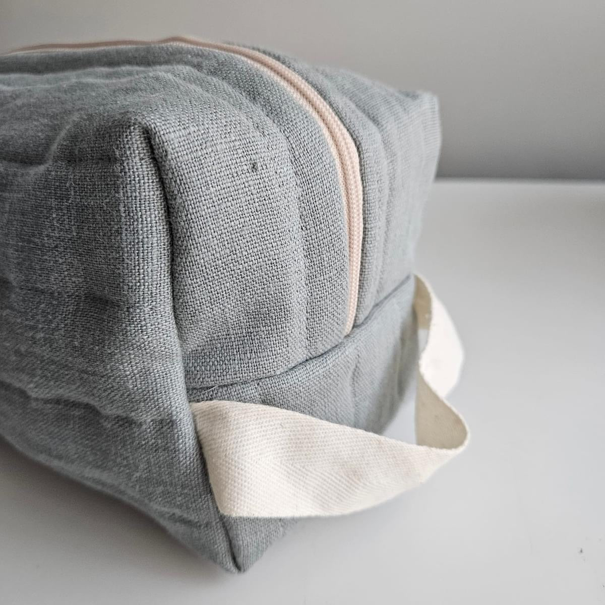 Gray fabric cosmetic bag with cream zipper and handle.
