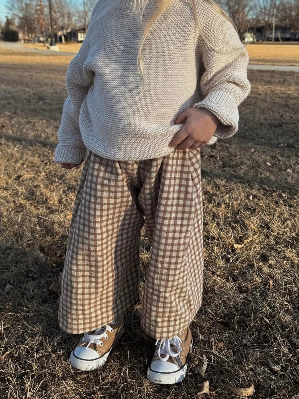 Child wearing a sweater and plaid pants, standing outdoors.
