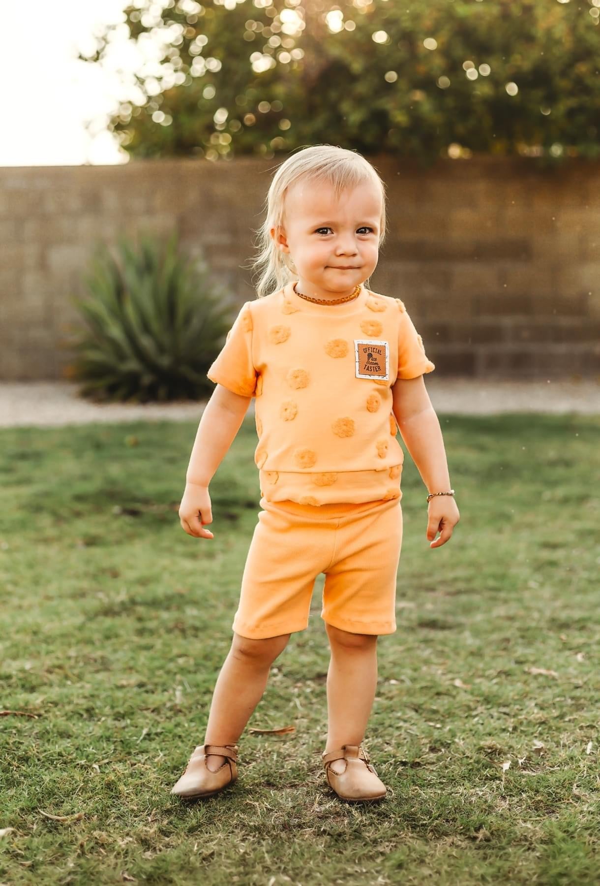 Young child wearing orange shorts and shirt.