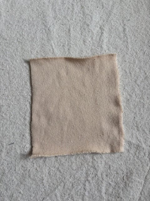 Beige fabric swatch on a textured gray surface.