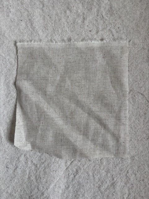 Square piece of light-colored fabric on a textured surface.