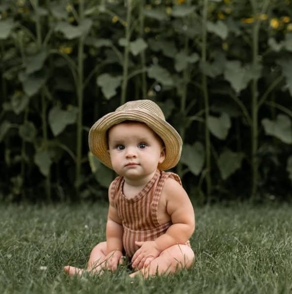 Baby in straw hat sitting in grass.