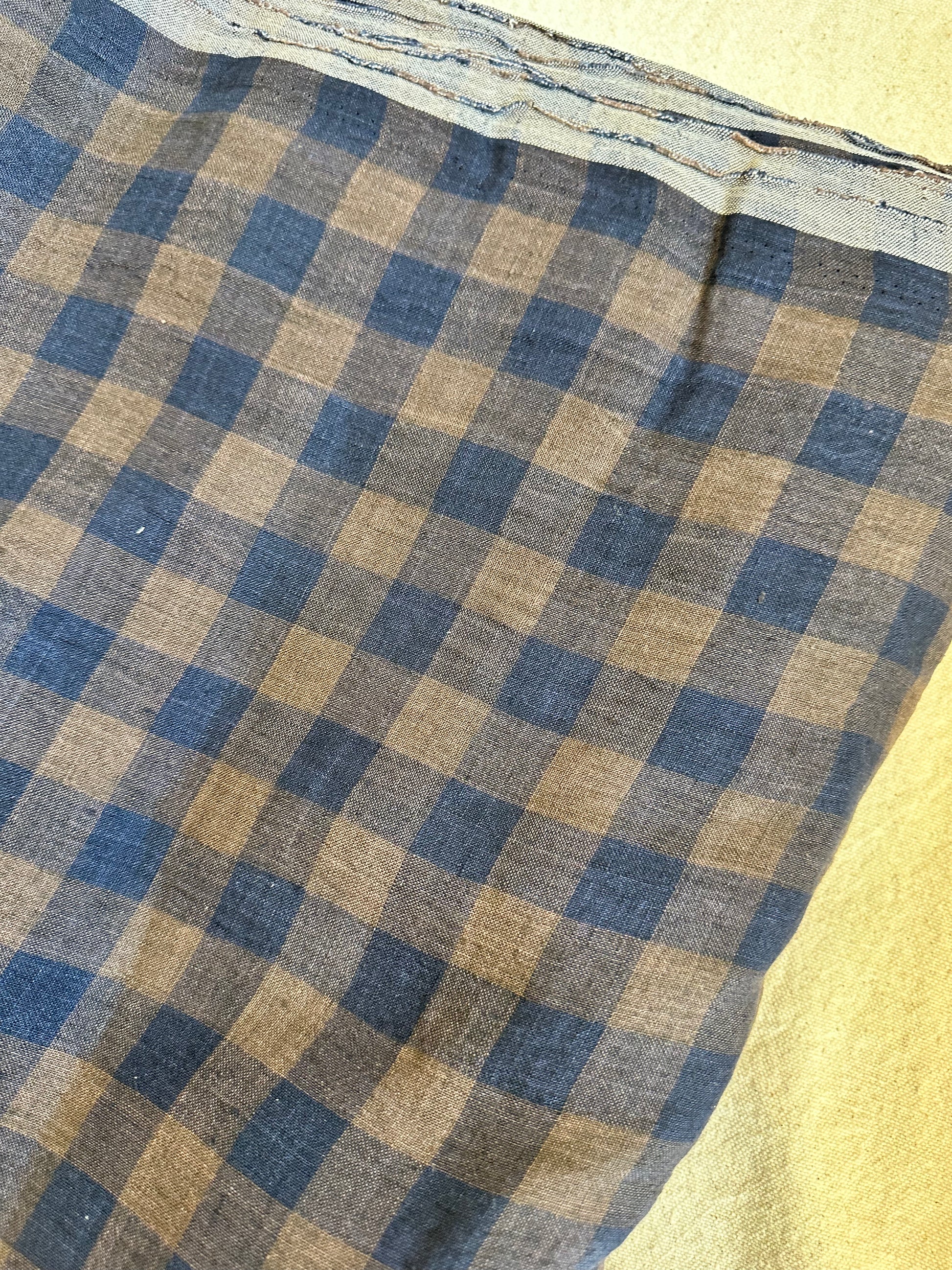 A close-up of a plaid fabric with a blue and tan checkered pattern, laid flat on a light beige surface.